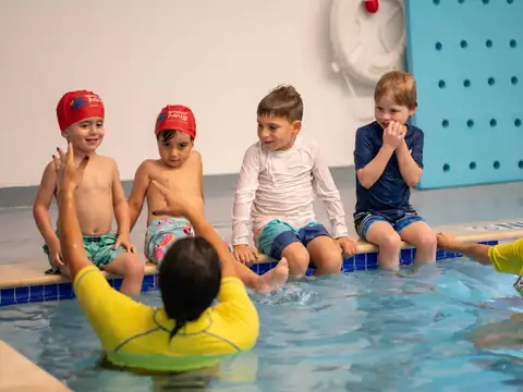 Kids with swim caps sitting by the pool with their instructor